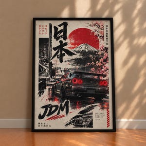 Puede incluir: Un póster enmarcado que muestra un coche deportivo negro con luces traseras rojas, un gran sol rojo, el monte Fuji y flores de cerezo. La obra incluye caracteres japoneses, el texto JDM y la frase Japanese Domestic Market en estilo gráfico.