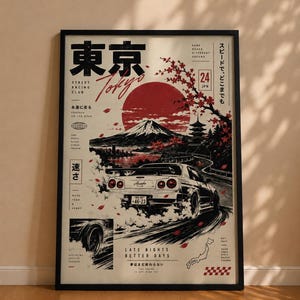 Könnte beinhalten: Ein gerahmtes Poster mit einem weißen Sportwagen, der auf einer Straße driftet, vor dem Hintergrund des Berges Fuji und einer großen roten Sonne. Das Design enthält Kirschblütenzweige, japanischen Text und englische Phrasen.