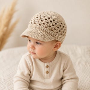 May include: A beige crochet cap featuring a textured granny square pattern on the crown and a solid brim. The cap is crafted from yarn and has a structured shape that covers the top of the head, providing a classic look with intricate stitching.