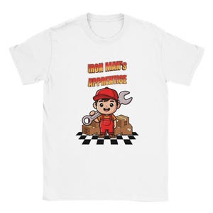 May include: White t-shirt with a cartoon mechanic holding a wrench, and the text "IRON MAN'S APPRENTICE". The mechanic wears a red cap and overalls, standing on a black and white checkered floor with cardboard boxes behind him.