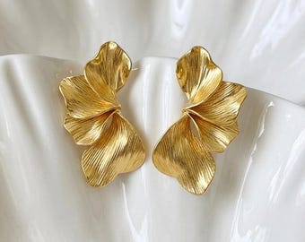May include: A pair of gold-toned earrings featuring a layered, fan-like petal design with a brushed, textured finish. Each earring consists of multiple overlapping curved segments that create a dimensional, organic shape resembling a blooming flower.