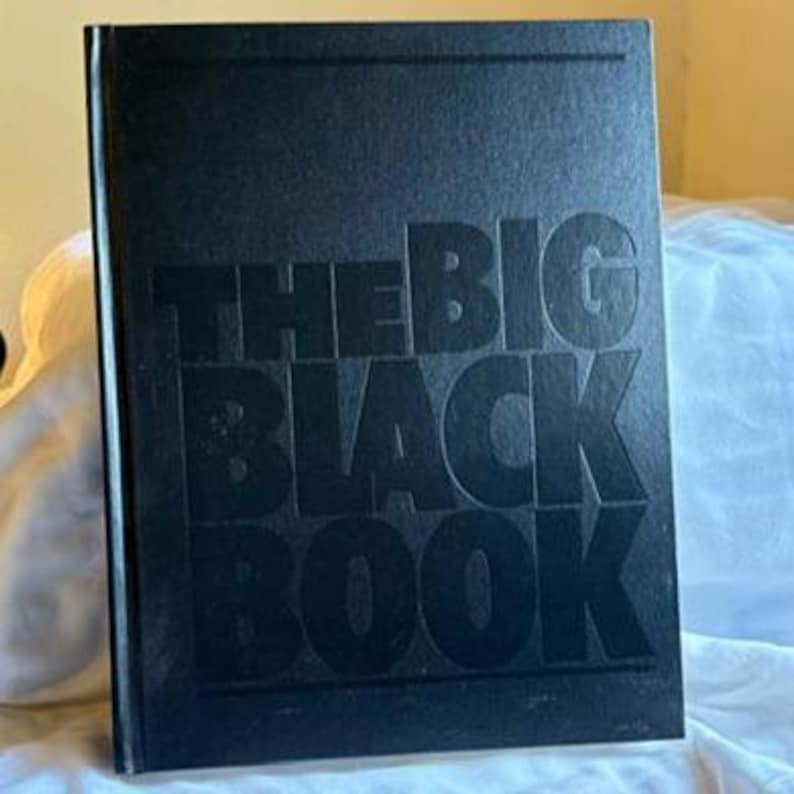 May include: A hardcover book titled "THE BIG BLACK BOOK" in embossed black lettering. The book is set against a soft, white background. The cover has a textured appearance.