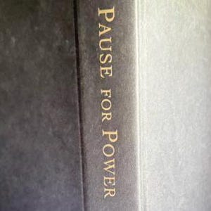 May include: A dark charcoal gray book cover featuring the text PAUSE FOR POWER printed in a vertical orientation in a serif gold font. The surface of the cover has a subtle, fine-grained texture, and the spine is visible on the right side.