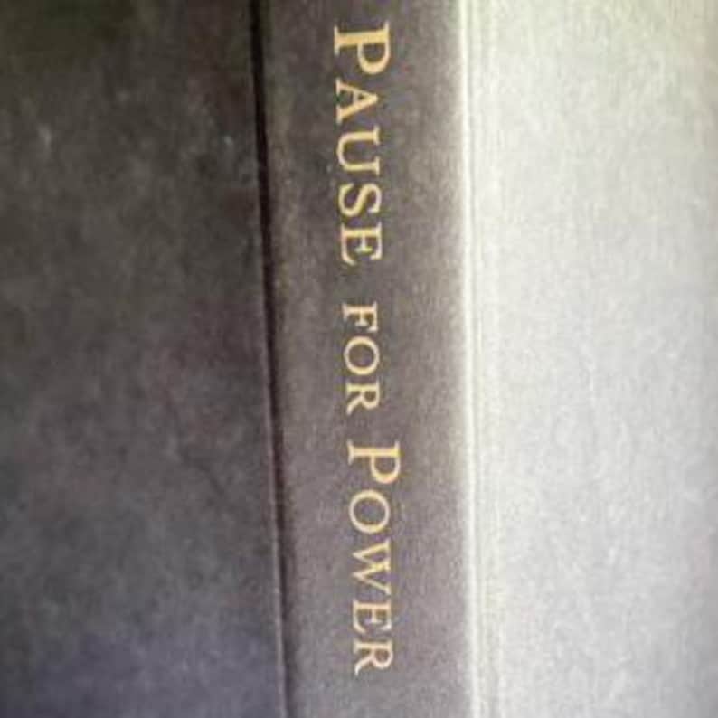 May include: A dark charcoal gray book cover featuring the text PAUSE FOR POWER printed in a vertical orientation in a serif gold font. The surface of the cover has a subtle, fine-grained texture, and the spine is visible on the right side.