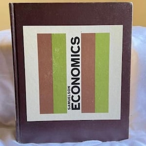 May include: A hardcover book titled "ECONOMICS" by Samuelson. The cover features a white rectangle with vertical stripes of brown and green. The book has a dark brown cover.