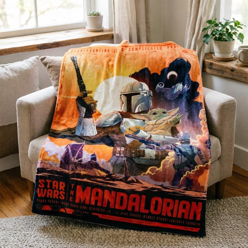 K&ouml;nnte beinhalten: Eine Star Wars: The Mandalorian-Decke mit dem Mandalorianer und Grogu. Die Decke hat ein lebendiges Design mit Orange-, Blau- und Schwarzt&ouml;nen. Die W&ouml;rter "STAR WARS" und "THE MANDALORIAN" sind deutlich sichtbar.