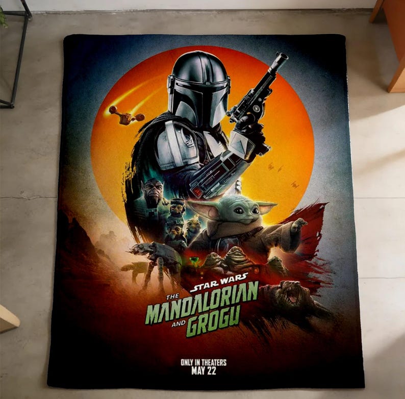 K&ouml;nnte beinhalten: Eine rechteckige Decke mit einer lebendigen Grafik von "The Mandalorian and Grogu". Das Design zeigt den Mandalorianer, Grogu und andere Charaktere vor dem Hintergrund einer orangefarbenen Sonne. Der Text "The Mandalorian and Grogu" ist deutlich sichtbar.