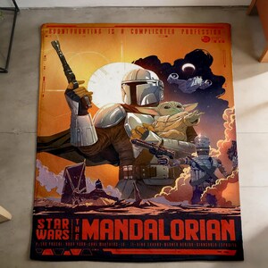 K&ouml;nnte beinhalten: Eine rechteckige Star Wars: The Mandalorian-Decke. Die Decke zeigt ein Design im Posterstil mit dem Mandalorianer, der eine Waffe und Grogu h&auml;lt. Die Decke ist &uuml;berwiegend orange, braun und schwarz mit den Worten "Star Wars" und "The Mandalorian".