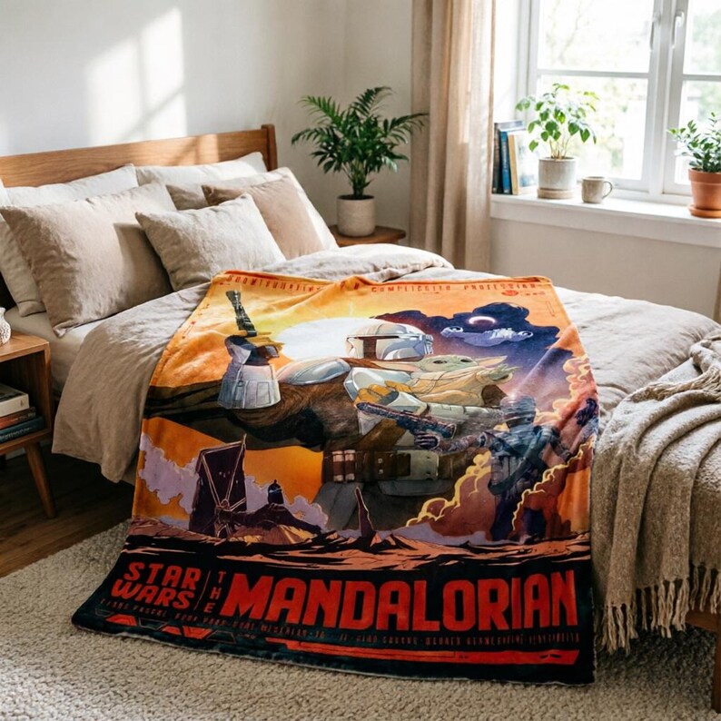 K&ouml;nnte beinhalten: Eine Star Wars: The Mandalorian-Decke mit einer farbenfrohen Grafik von Charakteren und Szenen der Show. Die Decke hat einen rot-schwarzen Rand mit dem Titel der Show. Die Decke wird auf einem Bett mit neutralfarbener Bettw&auml;sche pr&auml;sentiert.