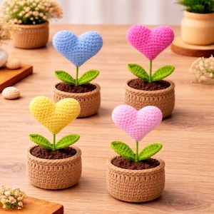 Peut inclure: Quatre fleurs en forme de cœur au crochet dans de petits pots bruns. Chaque fleur a un cœur de couleur différente : bleu, rose, jaune et rose. Des feuilles et des tiges vertes soutiennent les cœurs. Les pots sont remplis de terre brune.