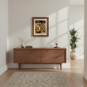 Op de afbeelding: Een ingelijste vintage print met de tekst "You are replaceable at work, but not at home" hangt boven een houten kast. De kast heeft twee deuren en staat op houten poten. Een patroonkleed ligt op de vloer.