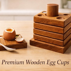 Könnte beinhalten: Eierbecher aus Holz und ein Löffel auf einer hellen Holzoberfläche. Ein Ei ist geöffnet und zeigt das Eigelb. Der Text "Premium Wooden Egg Cups" steht unten. Ein stapelbarer Eierhalter aus Holz ist ebenfalls vorhanden.