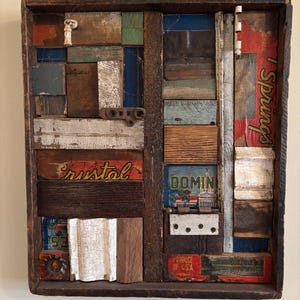 May include: A rectangular wooden art piece composed of various reclaimed wood pieces in shades of brown, blue, green, and white. The artwork includes the word "Crystal" and other text fragments. The piece has a rustic, collage-like aesthetic.