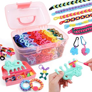 May include: A craft kit featuring a translucent pink plastic storage box filled with numerous small, colorful elastic hair bands. The set includes braided fabric bracelets, metal carabiner clips, a mermaid-shaped weaving loom, and a pink crochet hook.