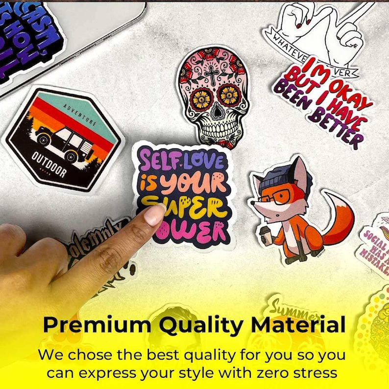 May include: A collection of colorful stickers with various designs, including a sugar skull, a fox with glasses, and text that reads "Self Love is Your Super Power." The stickers are on a light gray surface.