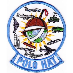 May include: Embroidered patch with a blue border and the words "POLO HAT". The patch features a brown hat over a globe, surrounded by various aircraft and military vehicles. The design includes yellow rays emanating from the globe.