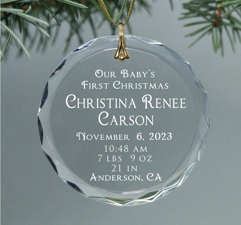 May include: Clear glass Christmas ornament with the text "Our Baby's First Christmas Christina Renee Carson November 6, 2023 10:48 AM 7 LBS 9 OZ 21 IN ANDERSON, CA"