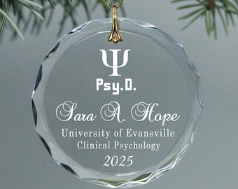 May include: A clear glass ornament with a gold ribbon and a gold hook. The ornament has a white inscription that reads "Ψ Psy.D. Sara A. Hope University of Evansville Clinical Psychology 2025".