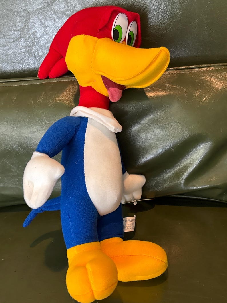 May include: A plush Woody Woodpecker doll. The cartoon character has a red head and beak, blue body, white chest and hands, and yellow feet. The doll has green eyes and a pink tongue. The doll is made of soft fabric.