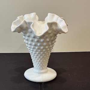 May include: A white ceramic mug with a black handle and the text "But First, Coffee" in a black, handwritten-style font. The mug is on a white surface.