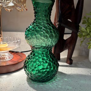 May include: A green glass vase with a textured, bubble-like pattern. The vase has a bulbous shape with a narrow neck and a wide base. The color is a vibrant, transparent green, and the vase is likely used for decorative purposes.