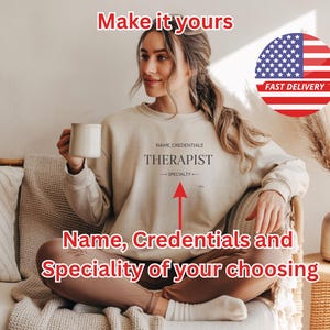 May include: A beige sweatshirt with the text "THERAPIST" and space for a name, credentials, and specialty. The image includes the text "Make it yours" and "Name, Credentials and Speciality of your choosing". A mug is held in the person's hand.