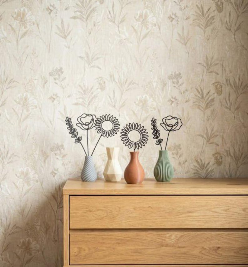 May include: A wooden chest of drawers with two drawers displays four small vases, each holding a wire flower sculpture. The vases are in blue, white, and brown. The background is floral wallpaper.