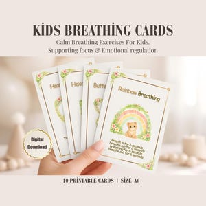 May include: A hand holding a set of Kids Breathing Cards. The cards feature calming breathing exercises for kids, supporting focus and emotional regulation. The cards have a gold border and include the text "Rainbow Breathing" with a rainbow and bear illustration. The cards are A6 size.
