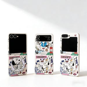 May include: Three white phone cases with a Snoopy cartoon design. Each case features a different Snoopy illustration and the word "Snoopy" in pink. The cases are designed for a flip phone.