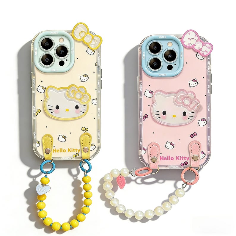May include: Two Hello Kitty phone cases, one pale yellow, the other pink. Both have a clear border with a repeating pattern and a bow at the top. Each case has a strap with a beaded wristlet and the words "Hello Kitty".