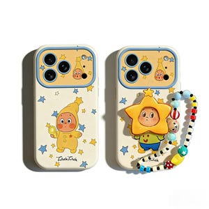 Puede incluir: Dos fundas para teléfono con diseños de personajes de dibujos animados. Una funda presenta un personaje con un atuendo amarillo sosteniendo una moneda de oro, la otra tiene un personaje en forma de estrella. Ambas fundas tienen un fondo crema con estrellas azules.