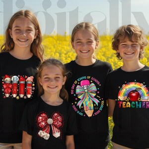 May include: Four children wearing black t-shirts with colorful school-themed designs. The designs include pencils, bows, and the word "Teacher" with a rainbow. The background is a field of yellow flowers.
