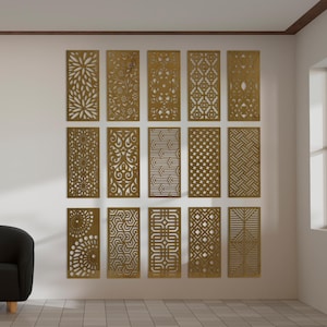 Op de afbeelding: Een verzameling van vijftien rechthoekige decoratieve panelen met ingewikkelde uitgesneden ontwerpen. De panelen hebben verschillende patronen, waaronder bloemen en geometrische vormen, en zijn op een witte muur gemonteerd. De panelen zijn goudkleurig.