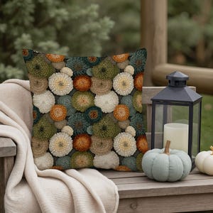 May include: A square throw pillow featuring a dense, repeating pattern of spherical, textured flowers in shades of burnt orange, sage green, teal, and cream against a dark background. The floral design covers the entire front surface of the pillow.