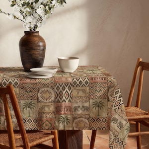 May include: A rectangular tablecloth with a repeating pattern of squares featuring suns, palm trees, elephants, and leopards in shades of brown, green, and red. A brown vase with white flowers, white plates, and a bowl are on the table.