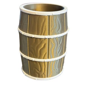 May include: A decorative barrel-shaped container with a gold finish and white trim. The container has a textured wood grain appearance and is banded with three white rings. The top and bottom edges are also trimmed in white.