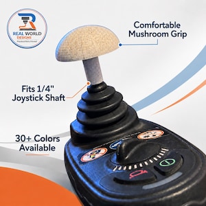 May include: A black joystick with a mushroom-shaped grip. The joystick has a gray shaft and a beige top. The text "Fits 1/4" Joystick Shaft" and "30+ Colors Available" are visible. The product is from Real World Designs.