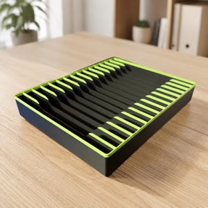 Puede incluir: Una bandeja organizadora de cajones rectangular con base e interior negros y detalles en verde lima brillante a lo largo de los bordes superiores. La bandeja está dividida en múltiples ranuras paralelas para organizar objetos planos.