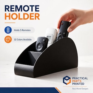 May include: A black remote holder with the text "REMOTE HOLDER". The holder is designed to hold five remotes. The image shows a hand placing a remote into the holder. The product is available in 32 colors.