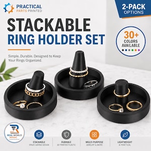 Peut inclure: Un ensemble de trois porte-bagues noirs, chacun doté d'une base circulaire et d'un cône central pour présenter des bijoux. Le texte indique Practical Parts Printed, Stackable Ring Holder Set, 2-Pack Options, 30+ Colors Available et Real World Designs.
