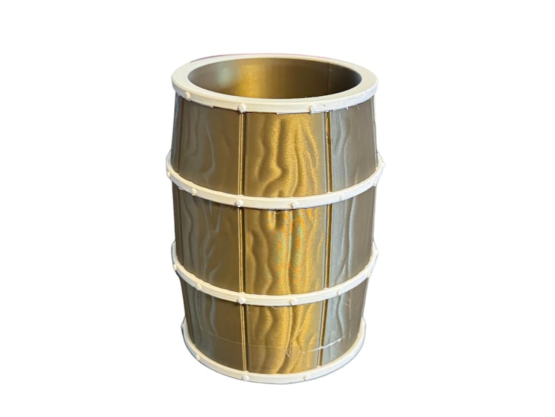 May include: A gold-colored barrel-shaped container with a white rim and bands. The container has a wood grain texture and is designed to resemble a traditional barrel. The bands are white and encircle the barrel.