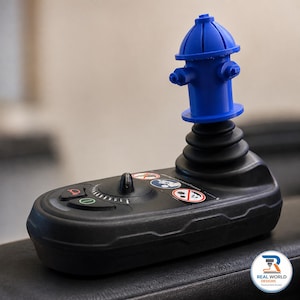 May include: A black wheelchair joystick controller featuring a blue fire hydrant-shaped handle topper. The base includes a circular speed dial, a horn button, a power button, and three circular safety warning icons with red borders and black graphics.