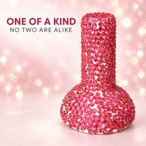 Puede incluir: Un objeto con forma de botella completamente cubierto de pequeños cristales rosas reflectantes. El texto ONE OF A KIND NO TWO ARE ALIKE está impreso en letras de color rosa oscuro sobre el objeto. La superficie está densa de piedras rosas.