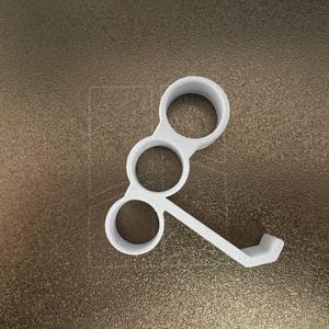 May include: A white 3D-printed object with three circular openings and a small, angled extension. The object is designed to hold multiple items. The background is a textured, metallic brown surface.