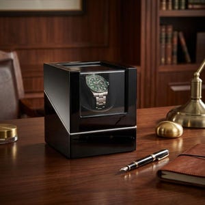 May include: A glossy black watch winder with a silver trim, showcasing a green and silver wristwatch. The winder is on a wooden desk, with a pen, notebook, and other items. The watch winder is a stylish accessory.