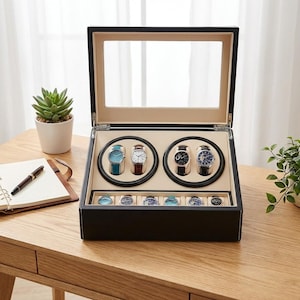 Op de afbeelding: Een zwarte horlogewinder met een glazen deksel, met vier automatische horloges. Het interieur is beige, met individuele horlogehouders. Daaronder een compartiment met zes extra horlogedisplays. Op een houten oppervlak.
