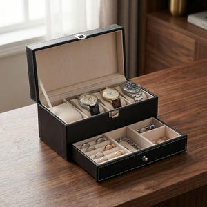 Può includere: Una scatola in pelle nera per orologi e gioielli con interno beige. La sezione superiore contiene quattro orologi, mentre il cassetto inferiore contiene anelli e altri gioielli. La scatola è su una superficie di legno.