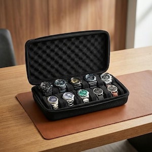 Op de afbeelding: Een zwarte horlogekoffer met ritssluiting, open om tien diverse polshorloges te onthullen. De horloges hebben verschillende band- en wijzerplaatkleuren, waaronder zilver, zwart en bruin. De koffer staat op een bruine leren bureaumat op een houten bureau.