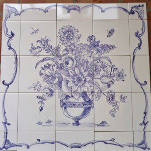 May include: A blue and white ceramic tile with a hand-painted design of a bouquet of flowers in a vase. The flowers are in shades of blue and purple, and the vase is a classic urn shape.