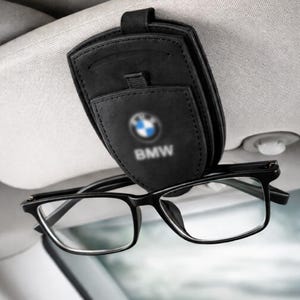 以下が含まれることがあります： BMWのロゴが入った黒い革製のカーバイザーサングラスホルダー。ホルダーはカーバイザーに取り付けられており、黒いフレームの眼鏡を1組収納できます。メガネはクリアレンズです。